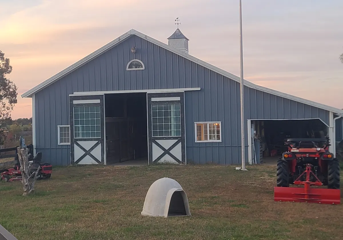 The gray main barn at Sunny Hills Farm with a cupola and white cross-buck doors